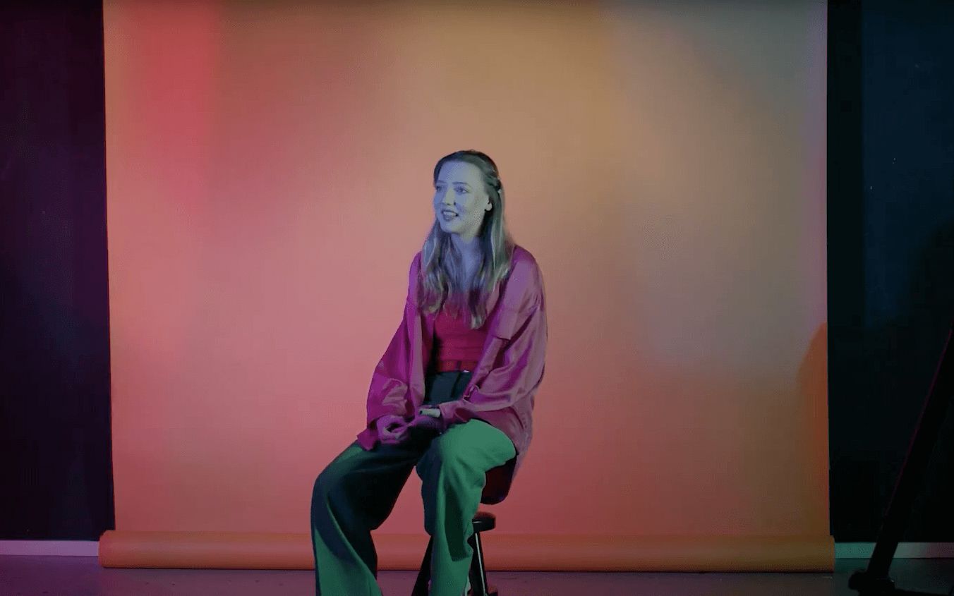 a girl sitting in front of a camera with a colourful vibe