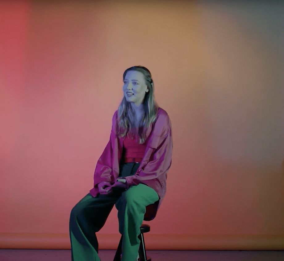 a girl sitting in front of a camera with a colourful vibe