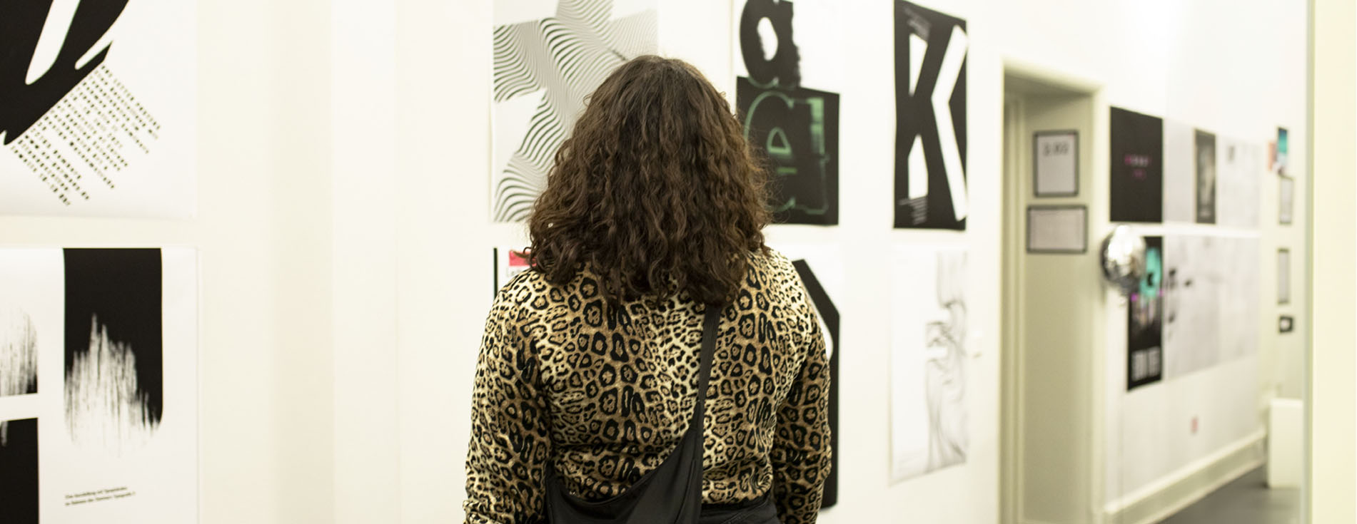 a girl with animal print shirt standing in front of a wall of graphic design poster
