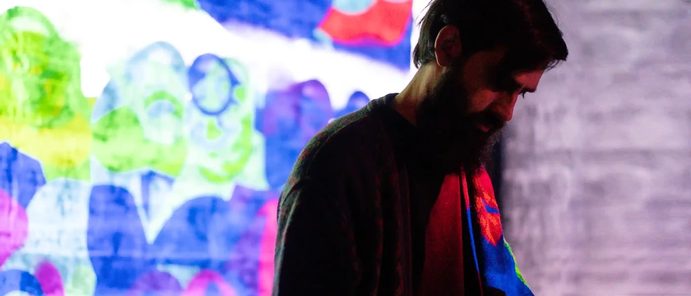 a man with a beard standing in front of a colorful background