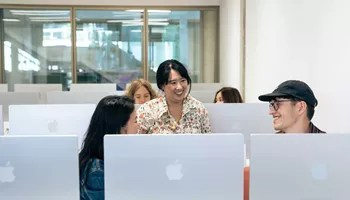 a bunch of people sitting and standing in a room full of computer