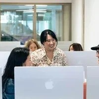 a bunch of people sitting and standing in a room full of computer