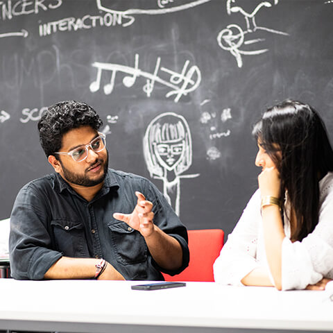 a man and a woman sitting at a table in front of a chalkboard