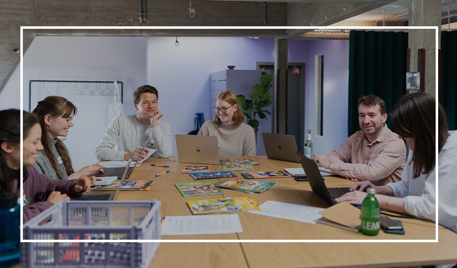 a group of people sitting around a table with laptops