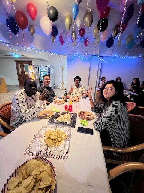 a group of people sitting at a table with food and balloons